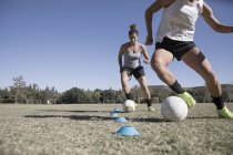Due giovani donne dribbling palloni da calcio sul campo da calcio — Foto stock