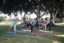 Colegialas practicando yoga guerrero tres posan en el campo deportivo de la escuela - foto de stock