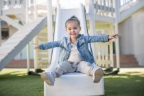 Chica en preescolar, retrato sentado en el tobogán del patio en el jardín - foto de stock