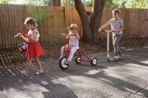 Três crianças em mini desfile, batendo tambor, montando triciclo e usando scooter — Fotografia de Stock