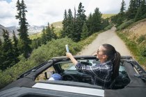 Молода жінка на дорозі поїздки, приймаючи смартфон selfie подорож в кабріолет, Брекенрідж, Колорадо, США — стокове фото