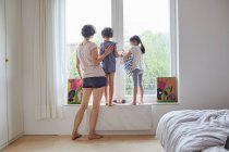 Mutter, Sohn und Tochter blicken aus dem Schlafzimmerfenster, Rückansicht — Stockfoto