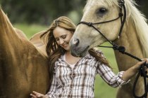 Mujer joven caminando con dos caballos, sonriendo - foto de stock