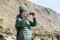 Donna con binocolo sulla costa rocciosa — Foto stock