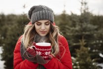 Retrato de mujer joven con café en el bosque de árboles de Navidad - foto de stock
