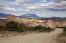 Camino desierto entre colinas que conducen a las montañas - foto de stock