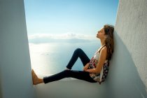 Mädchen sitzt auf Balkon mit Meer im Hintergrund, Santorini, kikladhes, Griechenland — Stockfoto