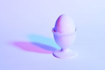 Яйцо в яичной чашке на фиолетовом фоне — стоковое фото