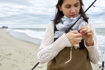 Young woman preparing fishing rod line on beach — Stock Photo