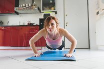 Portrait of young woman doing push ups on kitchen floor — Stock Photo