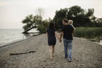 Vista trasera de una pareja paseando por la playa con su hijo pequeño, Lake Ontario, Canadá - foto de stock