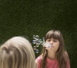 Two Girls blowing bubbles against hedge — Stock Photo