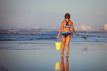 Vista trasera de la niña en la playa sosteniendo cubo, North Myrtle Beach, Carolina del Sur, Estados Unidos, América del Norte - foto de stock