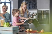 Mother and daughter looking in book for preparing food — Stock Photo