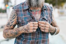 Tattooed male hipster fastening shirt buttons, cropped — Stock Photo