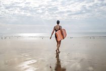Rear view of woman walking with surfboard on beach — Stock Photo
