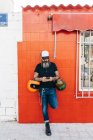Masculino hipster encostado contra vermelho parede olhando para smartphone — Fotografia de Stock