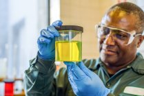 Lab technician looking at beaker of yellow biofuel in biofuel plant laboratory — Stock Photo