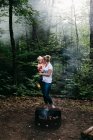 Madre llevando a su hija y besándola en la mejilla por la fogata forestal, Huntsville, Canadá - foto de stock