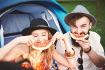 Young couple in trilbies making smiley face with melon slice at festival — Stock Photo