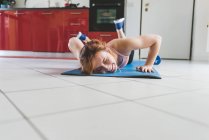 Young woman doing push ups on kitchen floor — Stock Photo