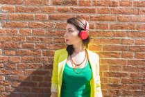Jeune femme dans les écouteurs à côté du mur de briques — Photo de stock