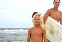 Portrait of mature male surfer and blond haired son on beach, Asbury Park, New Jersey, USA — Stock Photo