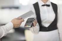 Официантка держит платежную машину по отношению к клиенту, клиент платит бесконтактным способом — стоковое фото