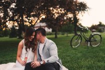 Jeune couple romantique avec champagne rose chuchotant dans le parc au crépuscule — Photo de stock