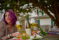 Ritratto di donna seduta a tavola con bottiglia di vino, bicchieri e cibo all'aperto — Foto stock