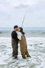 Pareja joven en vadeadores besándose mientras pesca de mar - foto de stock