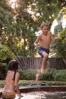 Jeune garçon sautant dans la piscine du jardin — Photo de stock