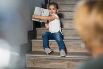 Menina nas escadas orgulhosamente mostrando desenhos de lápis de mãe — Fotografia de Stock