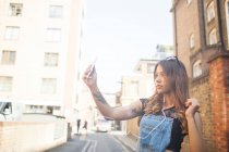 Молодая женщина на улице, делает селфи, используя смартфон — стоковое фото