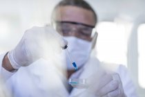 Trabajador de laboratorio usando pipeta, goteando líquido en la placa de Petri - foto de stock
