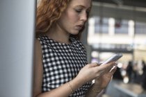 Side view of Young woman looking at smartphone against blurred background — Stock Photo