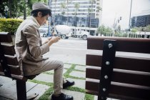 Jeune homme utilisant un smartphone sur banc — Photo de stock