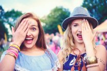 Portrait of two young female friends covering an eye at festival — Stock Photo