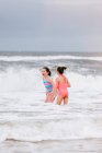 Две девушки, стоящие на океанских волнах, остров Дофин, Алабама, США — стоковое фото