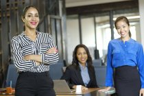 Portrait of three businesswomen in open plan office smiling at camera — Stock Photo