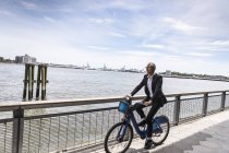Metà uomo d'affari adulto in bicicletta lungo il lungomare della città — Foto stock