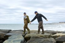 Young couple in waders walking over beach rocks — Stock Photo
