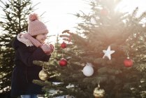 Girl looking at baubles on forest christmas tree — Stock Photo