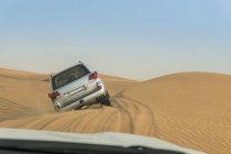 Off road vehicle driving over steep desert dunes, Dubai, Emiratos Árabes Unidos - foto de stock