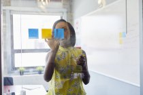 Junge Frau im Büro klebt Zettel an Glas im Büro — Stockfoto