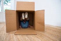 Garçon couché dans une boîte en carton avec les jambes levées — Photo de stock