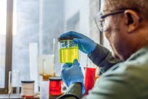 Lab technician inspecting beaker of yellow biofuel in biofuel plant laboratory — Stock Photo