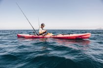 Young male sea kayaker looking at smartphone while fishing, Santa Cruz Island, California, USA — Stock Photo