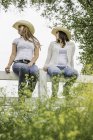 Молодые взрослые сестры в кокошниках сидят на заборе ранчо, оглядываясь назад, Бриджер, Монтана, США — стоковое фото