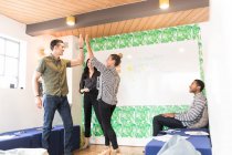 Group of businessmen and women high fiving in creative meeting room — Stock Photo